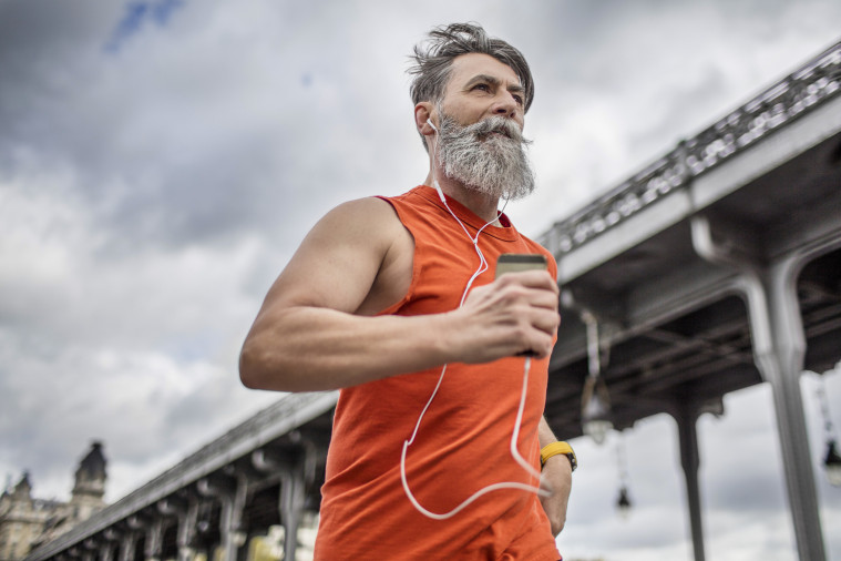 Homme quinquagénaire portant un débardeur orange et courant devant un pont en écoutant de la musique grâce à des écouteurs filaires.