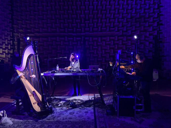 Photographie issue du concert dans la chambre sourde, on voit le mur tapissé de mousse en fond et des tapis à motifs au sol. La salle est baignée dans une lumière violette. A gauche, Laure Brisa est cachée par sa harpe. Au milieu se trouve Maud Geffray, derrière une table de mixage, un micro tendu vers elle. A droite, Christian Lahondes effectue les réglages de son 3D.
