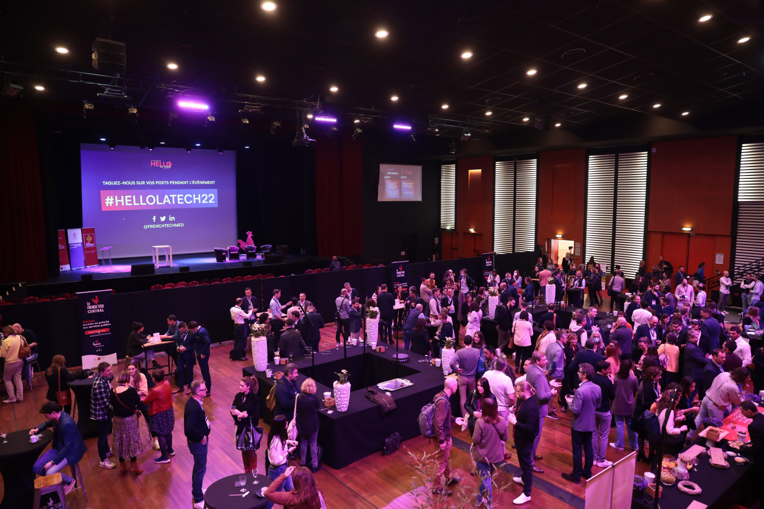 Photo des participants à l'événement Hello la tech : la salle est remplie et un PowerPoint projeté montre le hashtag de l'événement : #HELLOLATECH2022.